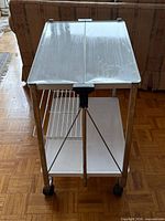 Front view of bar cart showing white top panels, chrome frame, wire shelf, lower shelf, casters