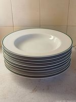 Stack of eight white pasta bowls with green rim