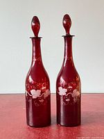 Full view of both cranberry glass decanters with stoppers