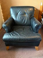 Front view of black leather armchair showing overall shape, wear on seat