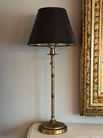 Full view of brass table lamp with black shade on surface