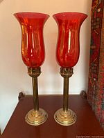 Full view of both ruby glass hurricane candle holders on brass bases