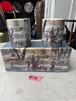 Two ceramic mugs showing winter hockey scene on top of original box