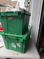 Pair of green plastic totes stacked, showing side panels, adhesive residue and wear