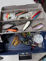 Open tackle box showing upper trays with spoon lures, spool of line and various tackle