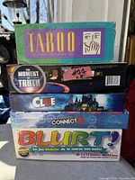 Stacked view of five boxed board games: Taboo, The Moment of Truth, Clue, Connect 4 sealed, Blurt!