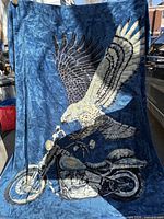 Front view of blue throw blanket with eagle and motorcycle graphic displayed hanging