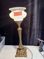 Full view of lit table lamp showing base, column and glass shade