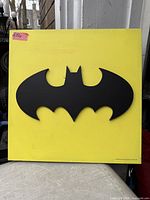 Front view of yellow square plaque with black Batman logo