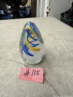 Full view of teardrop glass paperweight showing blue and yellow internal ribbons