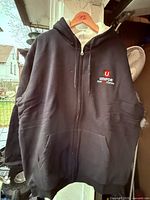 Front view of black Unifor zip hoodie on hanger showing logo and pockets
