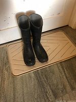 Full view of both black rubber knee-high boots standing on mat