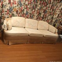 Front view of cream floral three-seat sofa with cushions and skirted base