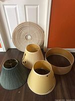 Five assorted lamp shades in various colors and conditions