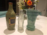 Front view of all three items: ceramic decorative bottle, clear Coca-Cola bottle, turquoise ceramic vase
