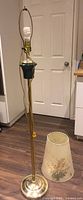 Full view of brass floor lamp, pole, base, harp, wiring, separate floral shade