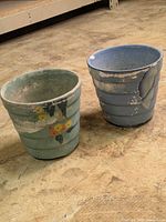 Two ribbed pottery flower pots showing exterior colours, floral painting and paint loss