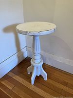 Full view of white distressed round pedestal table showing top, column and tripod feet