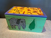 Closed box showing painted elephant, pear shape, yellow lid with symbols