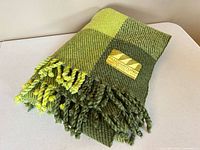 Folded green plaid wool blanket showing fringe and texture