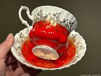 Underside of teacup resting in saucer showing red glaze, gold floral decoration, maker’s mark on base