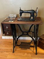 Full view of Singer treadle sewing machine in open position with attachments on tabletop