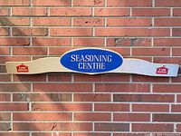 Full frontal view of entire wooden sign against brick wall showing overall design and logos