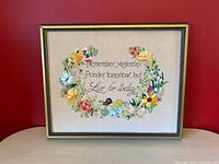 Front view of framed floral needlepoint showing full design and quote