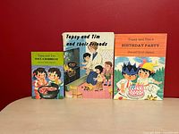 All three Topsy and Tim books standing side by side on table against red background