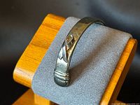 Cuff front on display stand showing raised ribbon motif and patina