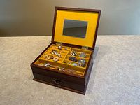Open jewelry box showing interior mirror, yellow felt compartments and assorted jewelry