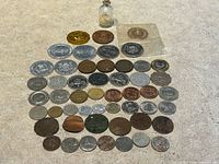 Overall view of entire lot showing approximately fifty coins/tokens, brass octagonal piece, sealed medallion, and coin in glass bottle