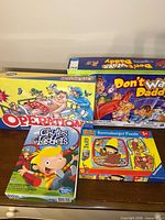 Group shot showing all four boxed items: Operation, Don’t Wake Daddy, Chutes & Ladders, Ravensburger Curious George puzzle