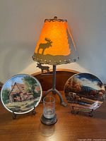 Group view of lamp, two plates on stands, and candle holder