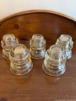 Five of the six glass insulators arranged on wooden surface showing overall appearance
