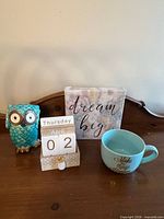 All four items grouped: owl figurine, perpetual calendar, sign, mug