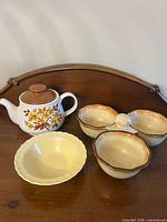 All three ceramic items on wooden surface: teapot, divided dish, yellow bowl