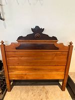 Full view of wooden headboard with carved crest and turned finials