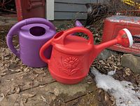 Red and purple plastic watering cans on ground