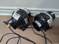 Two black 4-inch inline booster fans with power cords on floor