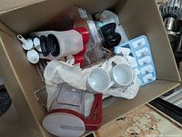 Box containing batter dispenser, silicone mold tray, measuring spoons, mugs and plastic container