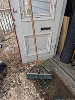 Full view of wood-handled push broom leaning against door