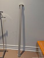 Full view of light gray square metal rail leaning against wall, mounting plates visible at top and bottom