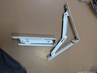 Two white folding shelf brackets showing hinged mechanism