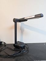 Full view of black adjustable desk lamp with attached power cord on tabletop