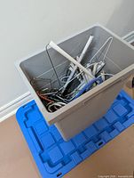 Grey tote on blue lid containing mixed wire and plastic hangers