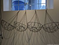 Four matching wire hanging baskets with chains displayed against wall