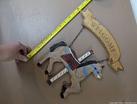 Overall view showing wooden arched "WELCOME" plaque, suspended painted wooden horse, tape measure for scale