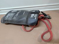 Jumper cables coiled with one clamp visible, inside black pouch showing printed safety info