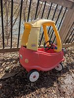 Left side view of Cozy Coupe showing red body, yellow roof, steering wheel, wheels
